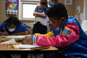 Profile view of a boy in a bright jacket writing